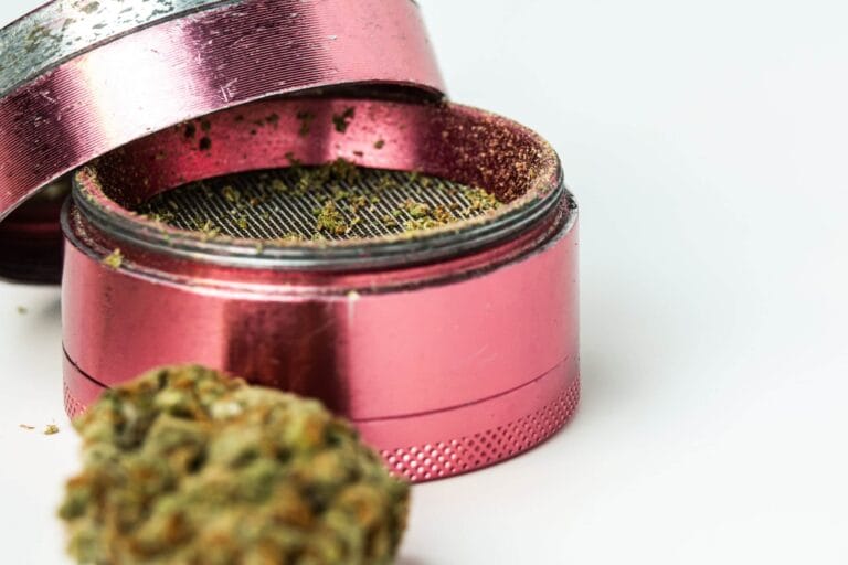 Otwarty różowy grinder z aluminium ze zmielonymi kwiatami CBD w komorze mielenia