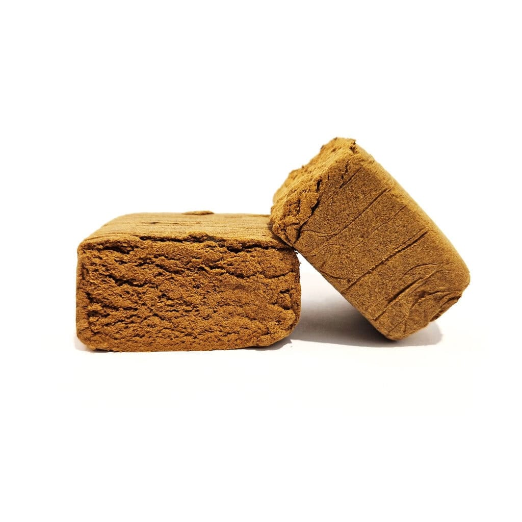 Deux morceaux de hash CBD brun doré de type pollen sur fond blanc