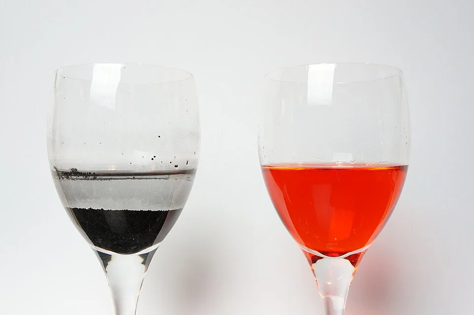 Deux verres : le charbon actif dans celui de gauche a retiré le colorant rouge encore visible dans celui de droite